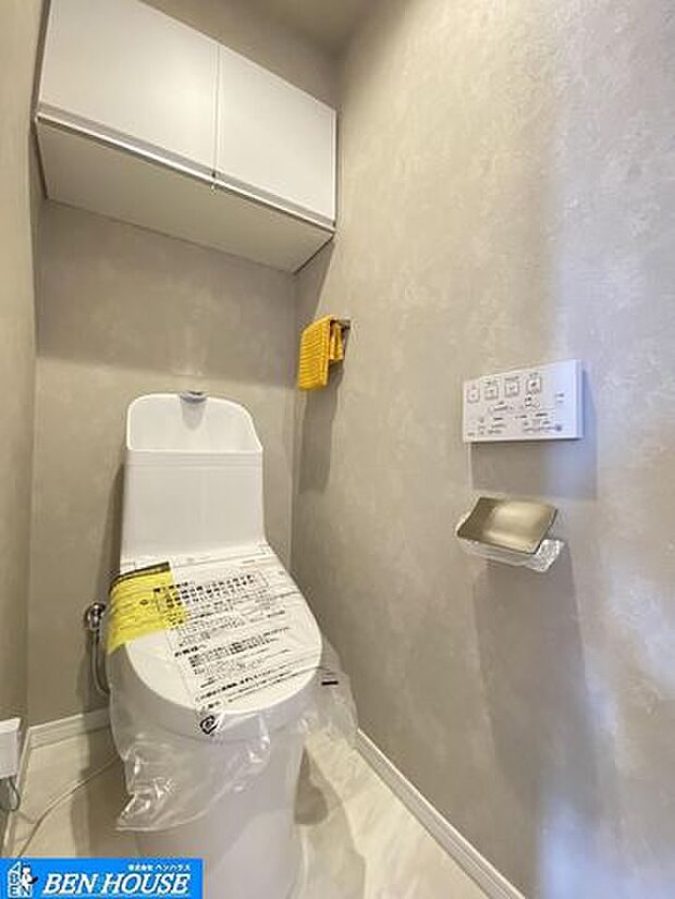 ・新規交換済のシャワー洗浄機能付のトイレ・清潔感が印象的な空間です・リモコンは壁掛けタイプでお手入れもしやすい設備です・吊戸棚の設置があり、トイレットペーパーやお掃除道具なども収納できます
