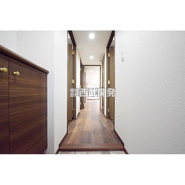 玄関からの廊下の様子。白を基調とし、床やドアは落ち着いた木目調で統一されています。