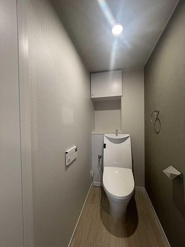 棚とタオルハンガーが便利なトイレ。アクセントクロスがクールな印象。