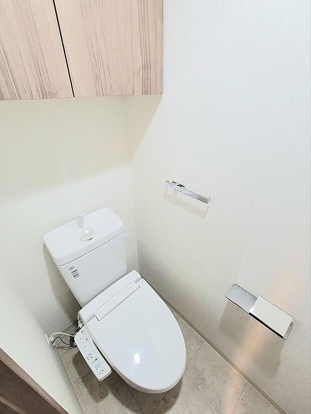 洗浄機能付暖房便座。トイレ上部には吊り戸棚が設置され、トイレットペーパー等をしまえます