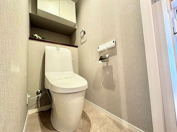 温水洗浄便座が備えられたトイレです。吊戸棚にトイレットペーパーや掃除用具などを収納し、すっきりとした空間を保ちます。