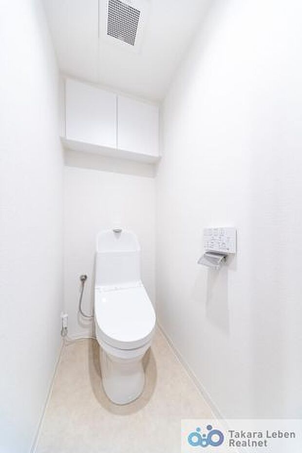 白を基調に清潔感のあるトイレ。トイレットペーパーホルダーとタオル掛けは標準で実装してます。上部に吊戸棚があり、掃除用具などの収納場所に困りません。