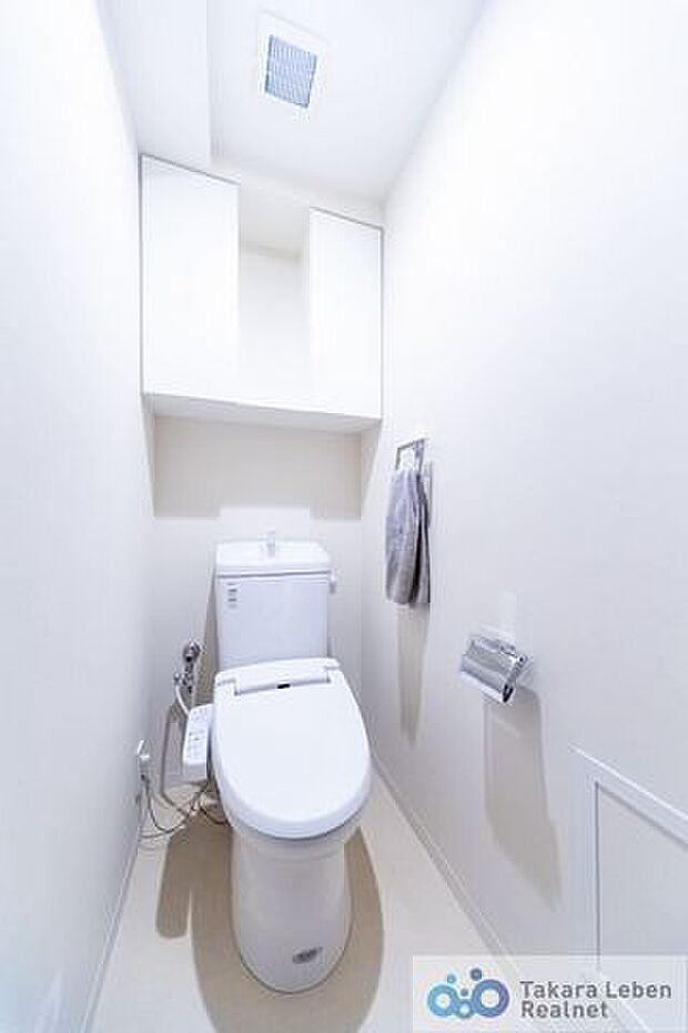 白を基調に清潔感のあるトイレ。トイレットペーパーホルダーとタオル掛けは標準で実装してます。上部に吊戸棚があり、掃除用具などの収納場所に困りません。カウンターもあるので、お洒落な空間に彩る事も出来ます。