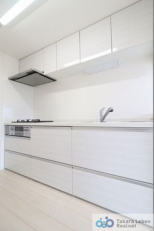 白の清潔感あるシステムキッチン。壁付け型のキッチンですが、横を向けばリビングの空間が広がり、明るく開放的。