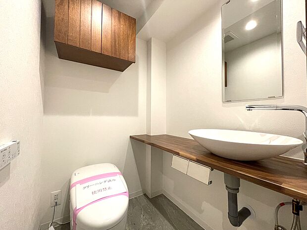 タンクレスですっきりとしたデザインのウォシュレット付きトイレです。室内は天然無垢材のぬくもりも感じる落ち着いた上質な空間です。吊戸棚も設置されており、トイレットペーパーなどの消耗品の収納ができます。