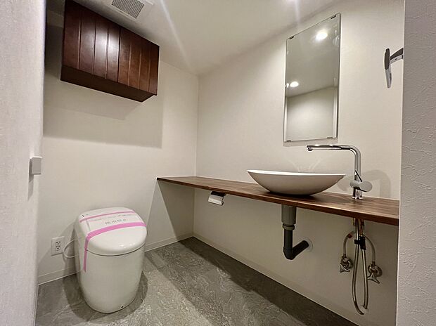 タンクレスですっきりとしたデザインのウォシュレット付きトイレです。室内は天然無垢材の温もりを感じる上質な空間です。吊戸棚も設置され、ミラー付の便利な専用手洗いスペースも付いています。【弊社施工事例】