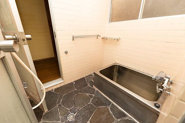 石張りの床が特徴的なお風呂です。壁にはタイルが張られています。窓もあるので、換気や掃除も面でも安心ですね。タオル掛けやシャンプー置きも設置されているのですっきりとした空間が維持できます。