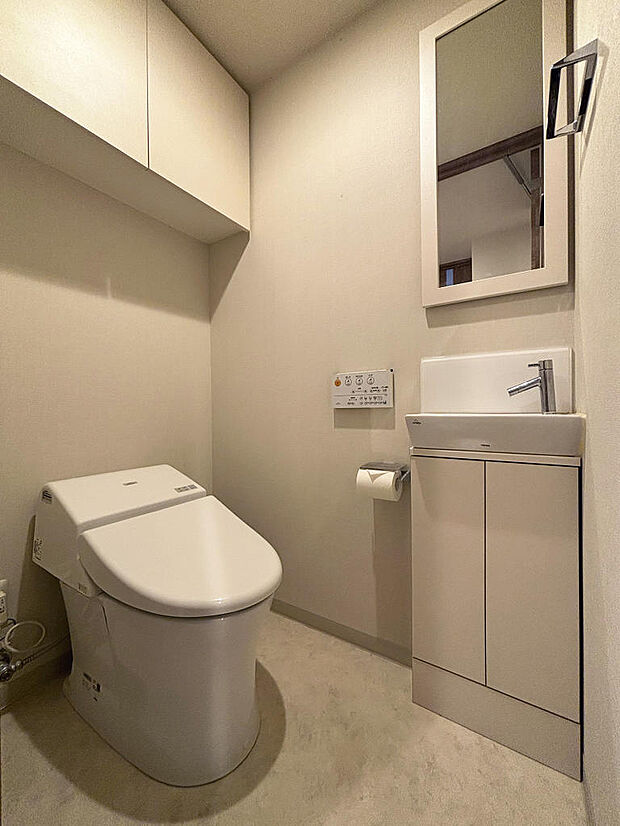 タンクレストイレ、手洗い器、鏡、吊り戸棚が配置されています。