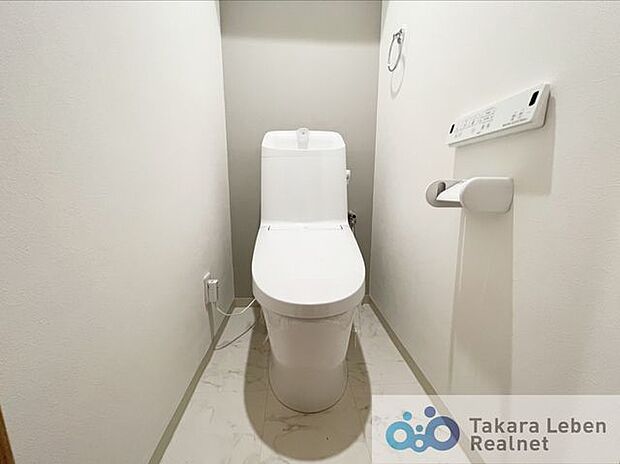 温水洗浄便座付トイレ。サイドには広く見せる白のクロス、正面には柔らかみを持たすグレーを使用。洗面室・トイレの床には汚れを目立ちにくくさせる大理石調を使用しています。