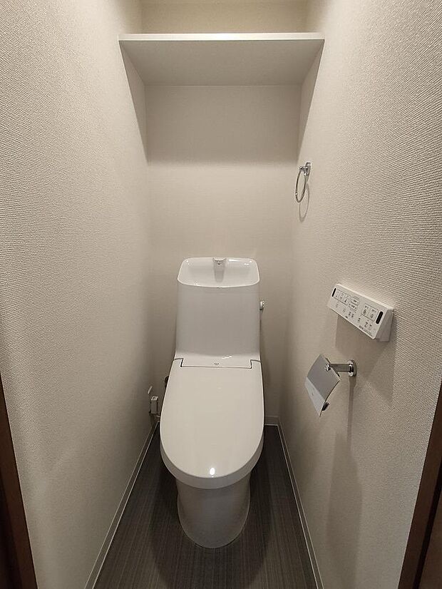 スタイリッシュな形状のトイレ。嬉しい頭上収納付き、ウォシュレットの操作パネルは壁に設置