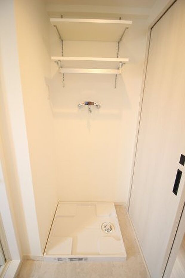 洗濯機置き場は壁の間に収まる邪魔にならない形。上部に棚があるのも便利です