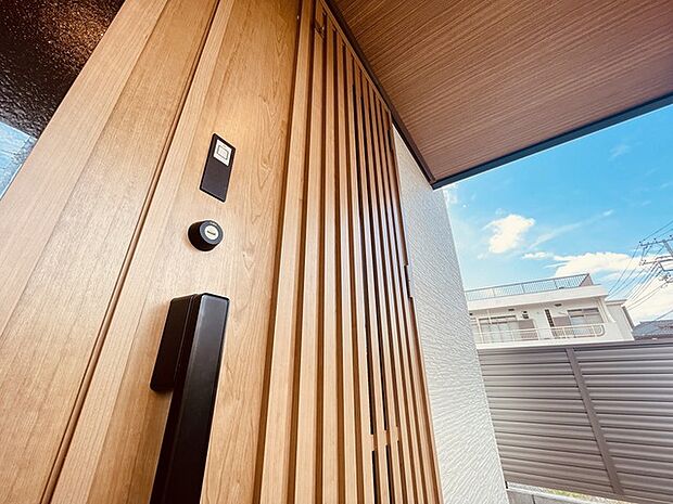 タッチキーを用いた玄関扉。木目調のデザインが景色とも調和がとれ落ち着いた外観スタイルを演出