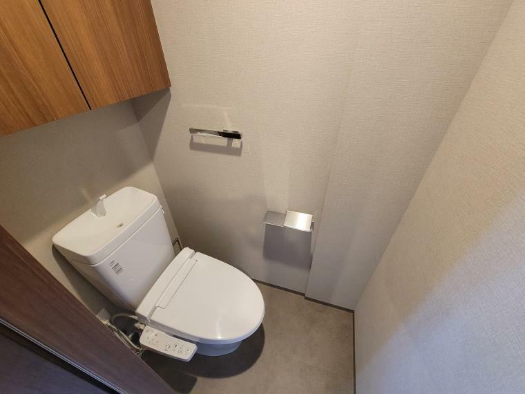 洗浄機能付暖房便座のトイレ。上部には吊り戸棚が設置されています。また扉が引き戸タイプで動線の妨げにならない設計となっています