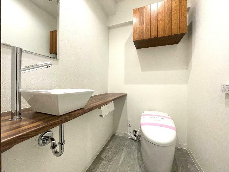 タンクレスですっきりとしたデザインのウォシュレット付きトイレです。室内は天然無垢材の温もりを感じる落ち着いた上質な空間です。吊戸棚も設置されており、トイレットペーパーなどの消耗品の収納ができます。ミラー付の便利な専用手洗いスペースも付いています。