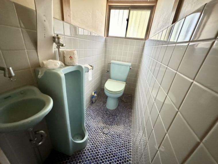 男性用トイレと洋式トイレが一緒に設置された、奥行きのあるトイレです。床に敷かれた紺色のタイルがいいアクセントになっています。窓があるので換気も十分にできます。手洗い器も設置され手洗いや掃除に便利です。