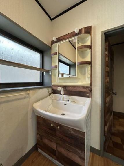【現地写真】洗面台の写真です。扉と合わせた木目調のデザインとなっています。
